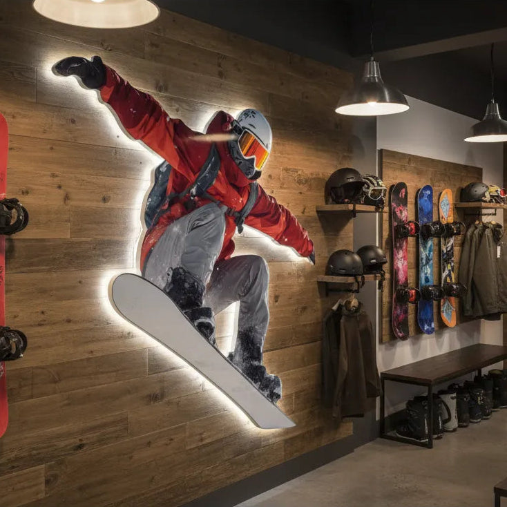 Snowboarding-themed store interior with a person in a red jacket and gray pants printed on a custom wall sign, jumping with a snowboard, surrounded by snowboarding gear.